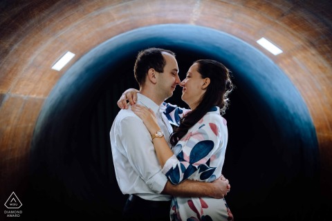 A romantic engagement photo was taken by a wedding photographer in Budapest, Hungary, capturing a couple embracing under the beautifully lit and arched tunnel at Budapest BME