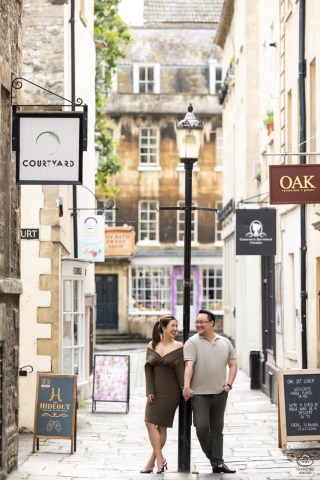 A couple in Bath, UK, posing for a portrait taken by a WPJA wedding photographer, standing with their backs against a city light pole in the streets