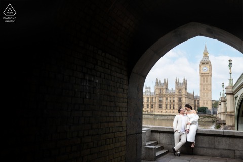 A couple in London, UK, poses for a portrait in the city, with a beautiful arch framing them and buildings in the background