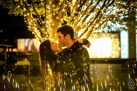 Christmas Love in the Heart of Washington DC: A Radiant Engagement Portrait The couple is standing together in front of Christmas lights in Washington DC, with reflections shining beneath them