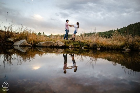 In the enchanting glow of the sunset at Evergreen Lake, the couple dances by the water's edge, holding hands. The serene lake mirrors their love, casting reflections that add a touch of interest.