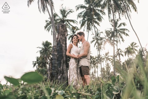 Near the beaches of Maceió, Brazil, a couple stands beneath towering palm trees. The lush greenery create a picturesque setting for their romantic picture, capturing the essence of their connection.