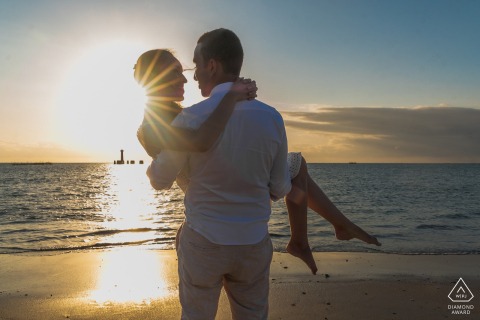 In Maceió, Brazil, a couple stands at the water's edge, bathed in the golden glow of the sunrise over the ocean. The tranquil seascape reflects the beauty of their connection, a romantic pose against the backdrop of the morning sky.