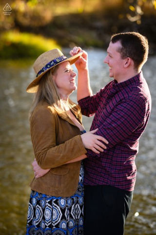 In Fort Collins, Colorado, a couple shares a warm hug amidst the vibrant colors of changing fall foliage. The rich hues of red, orange, and yellow leaves create a picturesque backdrop, capturing the essence of a romantic and autumnal scene.