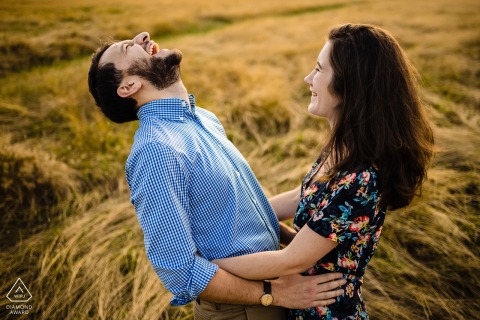 Portrait of a couple captured by a creative London wedding photographer in Richmond Park. The image shows a man with a wonderful big belly laugh facing his partner in tall grass.