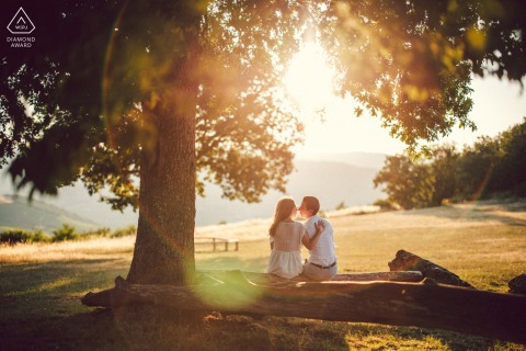 A couple portrait by a Rhônes wedding photographer, capturing a golden hour scene at sunset on top of Mont Brouilly in Beaujolais, with one hand on the shoulder, overlooking a simple and beautiful setting of a field.