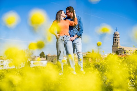 A couple engagement portrait captured by a Jaén wedding photographer in Baeza, Spain, showing a couple kissing in a yellow flower field under afternoon light.