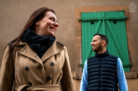 In Phalsbourg, France, a couple poses in front of heart-shaped green shutters for their engagement portrait, showcasing love and charm.