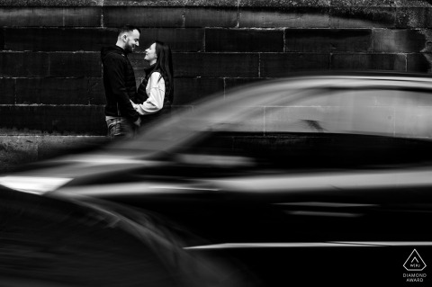 In Phalsbourg, France, a couple embraces each other as two cars pass by in black and white. The blurred portrait has a nostalgic vintage vibe.