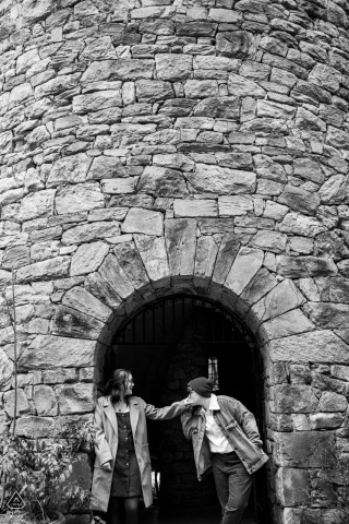 Captured at the Longwood Gardens, a monochromatic engagement portrait features a couple at the bell tower entrance. One tenderly kisses the other's hand, exuding a vintage charm.