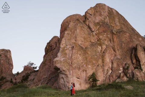 In this engagement portrait, a couple embraces in front of a majestic red rock formation in Boulder, CO, symbolizing their love and commitment against a breathtaking natural backdrop.