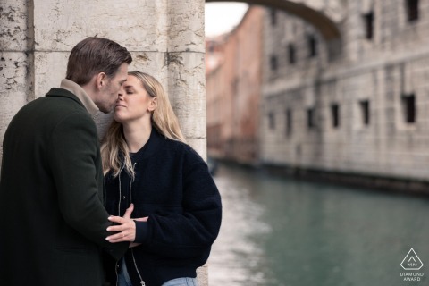 Capturing the intimacy after a a surprise proposal near the water by the Bridge of Sighs in Venice, a couple shares a sweet kiss in a tender embrace.