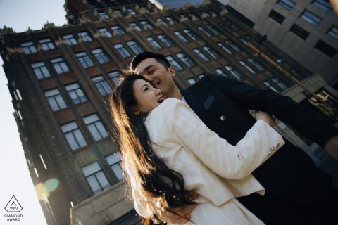 In their engagement portrait against the iconic backdrop of the Bund in Shanghai, China, the couple radiates joy with tall buildings framing the shot.