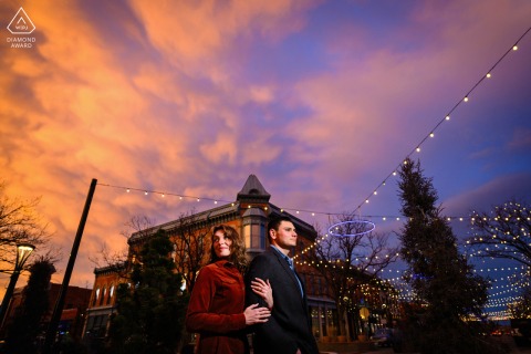 Embracing the romantic ambiance of Fort Collins, Colorado, this engagement portrait captures a couple in Old Town at sunset, with her tenderly holding his arm, beautifully illuminated by the photographer.