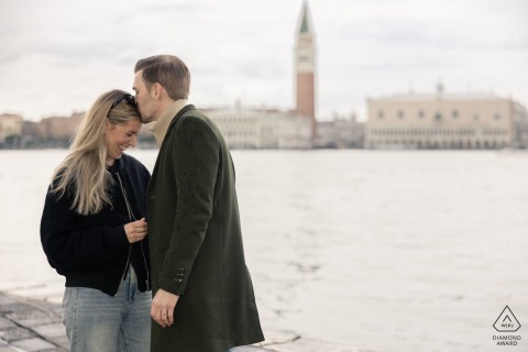A newly engaged couple embraces with a kiss on San Giorgio Island in Venice, near the water, capturing a second of love and joy.