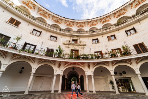 In beautiful Sevilla, Spain, this pre-wedding portrait captures a couple running and holding hands amidst stunning architecture in a wide shot.