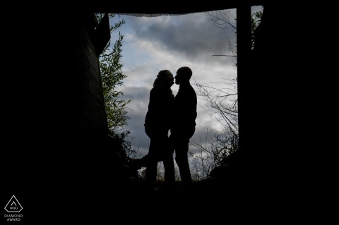 An engaged couple poses in a silhouette, gazing into each other's eyes against the cloudy skies of East Flanders, conveying their love and commitment.