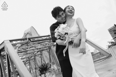 Shanghai Love: A couple shares a hug during their engagement portrait session at the iconic Bund in China. In this black and white shot, we see the man embracing his fiancée from behind, captured from a low angle view. 