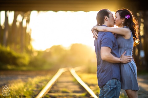 In the city of Santa Cruz California, the low afternoon sun shines behind their lovely kiss as they kiss on the rail tracks under the bridge. 