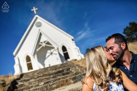 The engagement portrait features the couple in Tiburon, CA, sharing a sweet kiss in front of an old and quaint little white chapel, with a beautiful blue sky as their backdrop.