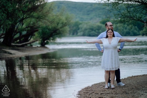 Engaged couple strikes a romantic movie-like Titanic pose at the water's edge in Hungary, Szigetcsúcs, captured by a skilled wedding photographer.