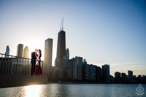 In Chicago's Milton Olive Park, a couple's engagement photo is beautifully captured at sunset, with the glowing horizon providing a stunning backdrop to their romantic scene.