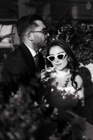 In the streets of Istanbul, a couple exudes hip style and urban vibes, wearing sunglasses. Captured in black and white, shadows are all around them under the bold sun, enhancing their edgy look.