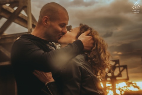 A couple shares a passionate kiss outdoors in Vierzon, surrounded by an autumn setting, capturing their joyful engagement.