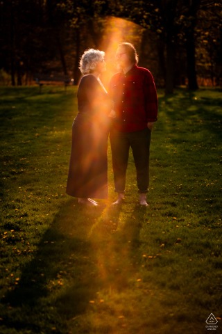 A couple stands in Rattray Marsh park with a sun flare stretching vertically across their bodies.