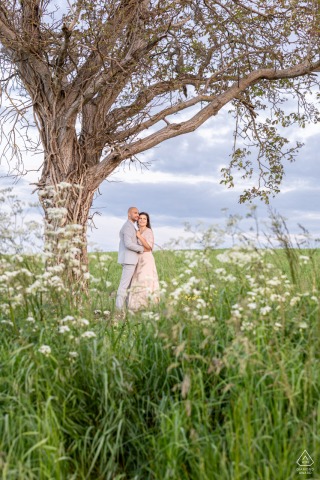 Wildflower Whimsy: Lovers' Romance Under a Tree in Chatellerault's Natural Beauty Lovers stand under a beautiful tree in Chatellerault, framed by colorful wildflowers, capturing a romantic, natural scene.