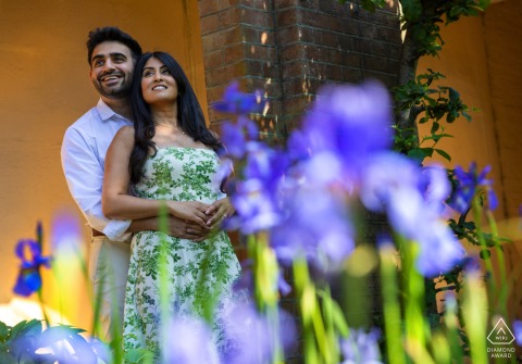 A couple in Hampstead Heath, London, captured from below with vibrant flowers adding color to the engagement portrait.