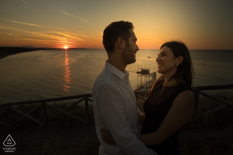 A couple embraces at sunset, overlooking the sea and the traditional fishing structure, "Trabocco," at Punta Aderci.