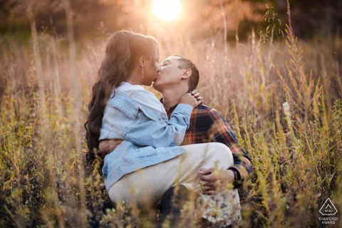 A couple embraces in tall grass at sunset, Tall Pines State Preserve, NJ, with a colorful sky illuminating the scene.