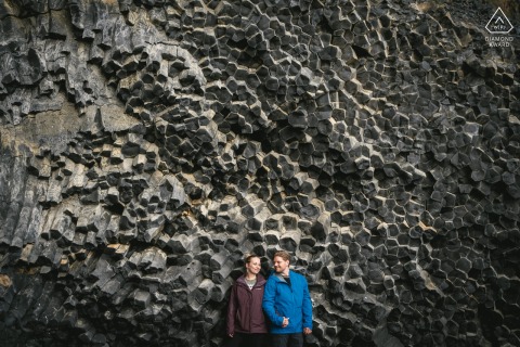 A joyful couple laughing, framed by Iceland's stunning south coast, stands before a dramatic geometrical basalt wall.