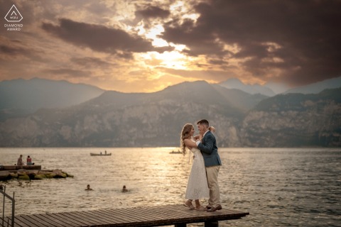 A couple lovingly embraces on a pier in Malcesine, Lake Garda, with a stunning sunset painting the sky behind them.