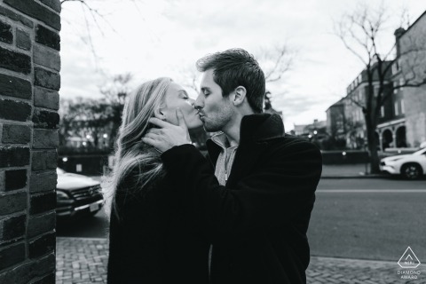 Kissing on Charming Street: Love Blooms Amid Historic Brick Buildings in Alexandria A couple shares a kiss on a charming street in Old Town Alexandria, surrounded by historic brick buildings.