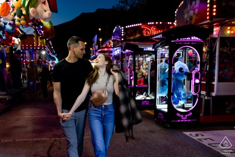Lovers walk hand-in-hand down the lively aisles of Grenoble's Foire des Rameaux, surrounded by vibrant lights and attractions.