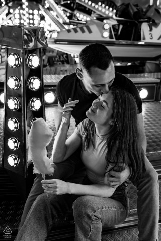 A couple shares a kiss, embracing lovingly at the vibrant Foire des Rameaux funfair in Grenoble.