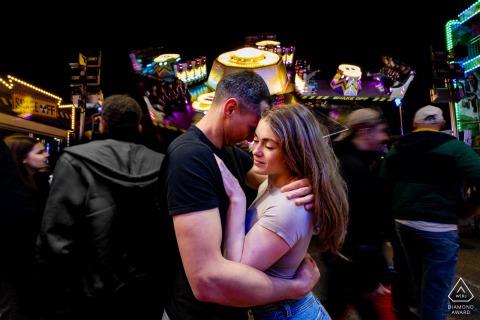 A loving couple embraces warmly before a brightly lit merry-go-round at Grenoble’s Foire des Rameaux.