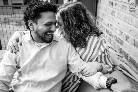 The couple shares an intimate laugh on their Minneapolis balcony, lost in each other during their engagement session, capturing a priceless memory.
