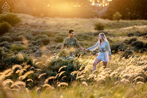 A couple walks hand in hand on Wassenaar's dunes at sunrise, surrounded by golden hues and gentle waves.