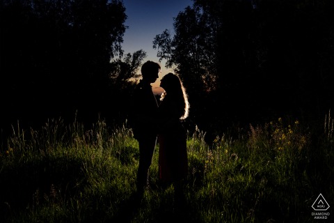 A couple stands closely together between tall trees at dusk in Bergschenhoek, soft twilight glowing.