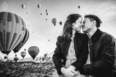 Couple sits nose to nose in Cappadocia, black and white photo, hot air balloons background.