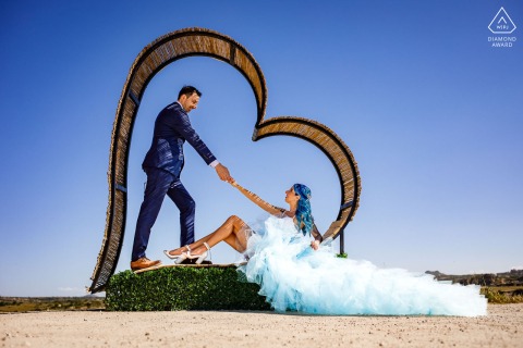 Couple in formal wear framed by large heart structure in Cappadocia desert during engagement session.