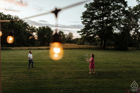 Engaged couple playing lacrosse joyfully in their Pennsylvania backyard at sunset, warm golden light.