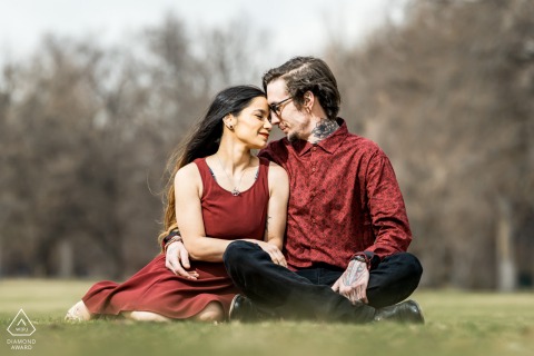 Couple in Denver, CO, USA, sitting cuddled together on grassy field, both wearing matching burgundy outfits, sharing an intimate photo session.