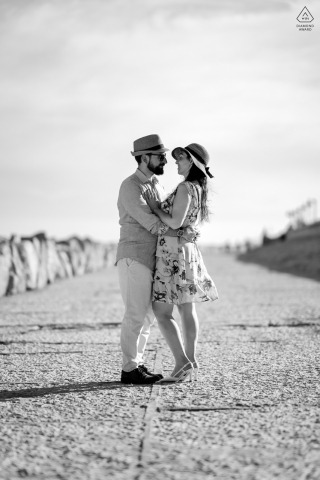 Couple Embraces On Jetty In Black-And-White Caorle Waterfront Seaside Photo Couple embraces on concrete jetty along Caorle, Venice waterfront; vertical black-and-white shot capturing intimate, seaside embrace..