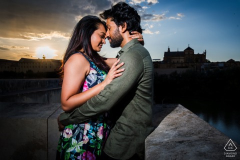Pre-wedding couple in Córdoba, Spain; standing head to head in intimate pose, photographer’s lighting, dramatic sunset in background.