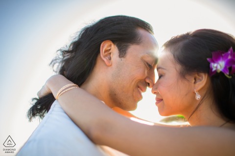 Sunlit Warmth: Engaged Couple’s Tender Close-Up With Glowing Santa Cruz Sunset Engaged couple in Santa Cruz, close-up with heads touching, sun shining behind them, creating a warm, glowing effect.