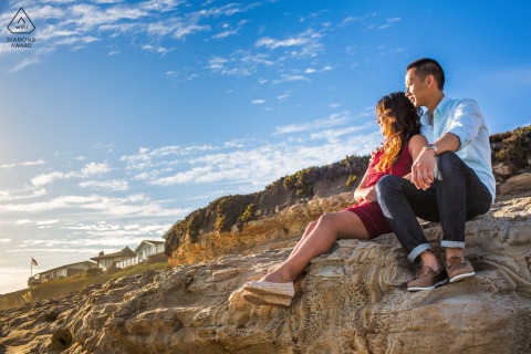 Engaged couple cuddling warmly on windswept bluffs in Santa Cruz, California, overlooking dramatic coastline.